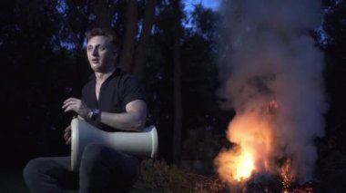 Yakışıklı adam bir peri ormanında ateşin etrafında oturur ve davul çalar