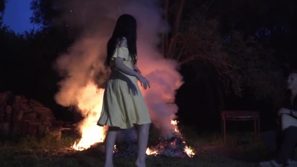 ハンサムな男が夜に森の火の近くで太鼓を打ち美しい少女が踊る — ストック動画