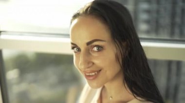 Güzel bir kız güzel manzaralı, yüksek bir evin penceresinin yanındaki kameraya poz veriyor.