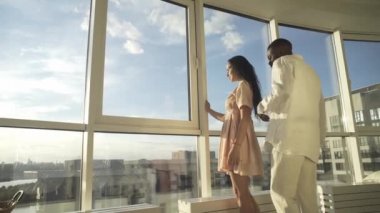 Yakışıklı siyah adam, güzel açık tenli kızı kucaklıyor pencere kenarında oturuyor, güzel bir manzarası var.