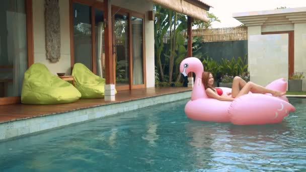 Femme couchée sur un grand flamant rose gonflable dans la piscine — Video