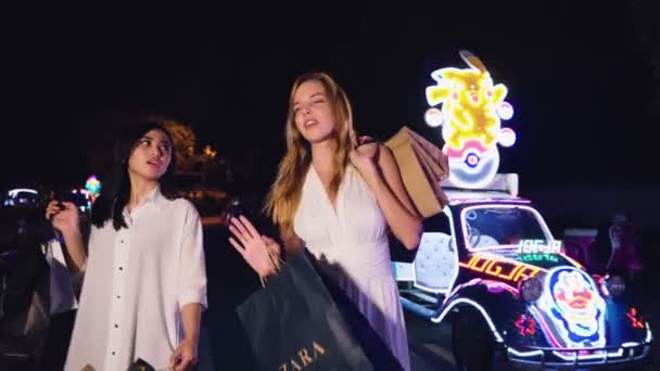 Две женщины, идущие по блестит автомобилей площади — стоковое видео