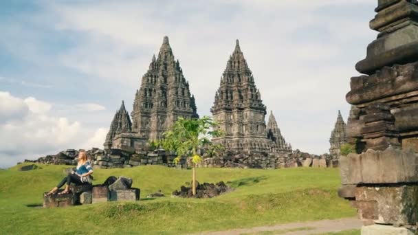 Woman sitting on stones in front of Prambanan temple — Stock Video