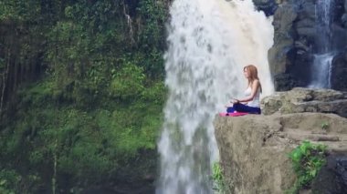 Yoga nilüferinde oturan kadın Tegenungan Şelalesinin yanında poz veriyor.