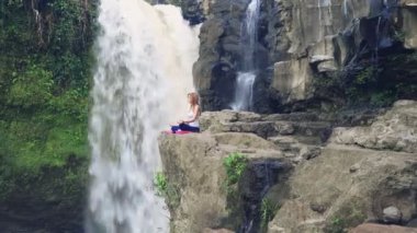 Yoga nilüferinde oturan kadın Tegenungan Şelalesinin yanında poz veriyor.