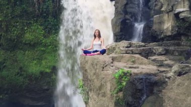 Yoga nilüferinde oturan kadın Tegenungan Şelalesinin yanında poz veriyor.