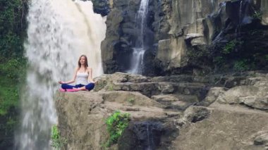Yoga nilüferinde oturan kadın Tegenungan Şelalesinin yanında poz veriyor.