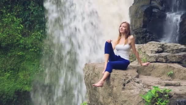 Woman sitting on a cliff next to Tegenungan Waterfall — Stock Video