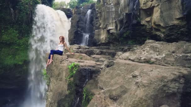 Mulher sentada em um penhasco ao lado da cachoeira de Tegenungan — Vídeo de Stock