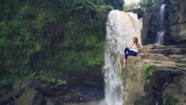 Femme assise sur une falaise à côté de la cascade Tegenungan — Video