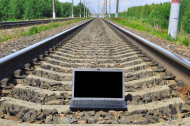 Black laptop on railway tracks. Travel industry. Railway going into the distance.