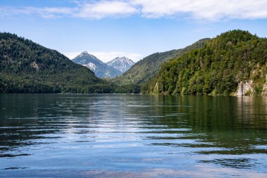 Mavi gökyüzü ve bulutlarıyla sessiz dağ gölü