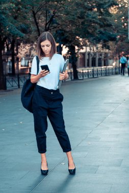 Şehir sokaklarında dizüstü bilgisayarı ve akıllı telefonu olan bir iş kadını.