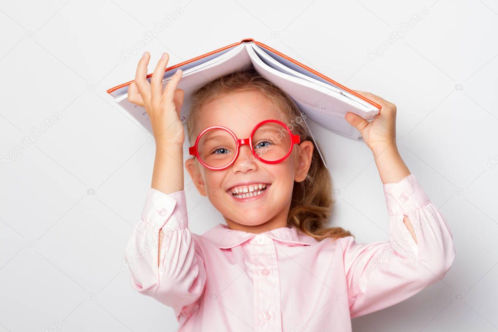 ittle girl preschooler wearing glasses keeps an open book on her head