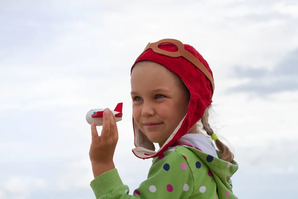 En liten flicka i badmössa piloter spelar i ett litet trä plan. — Stockfoto