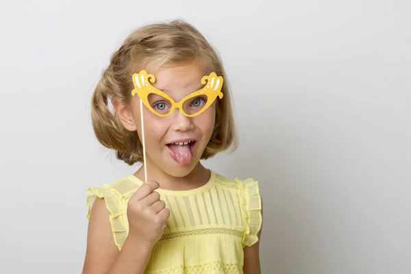 Menina engraçada com acessórios de papel. criança segurando óculos no pau . — Fotografia de Stock