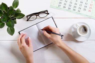 Kontrol listesi için maket, arka planda kalem ve kahve fincanı olan boş not kağıdı. Ofis, yazar ya da çalışma konsepti. Kalemle kadın eli.