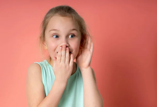 Studio portrait of pretty little child girl in blue dress with palm near her ear. She covers her mouth with her hand in surprise. — Stock Photo, Image