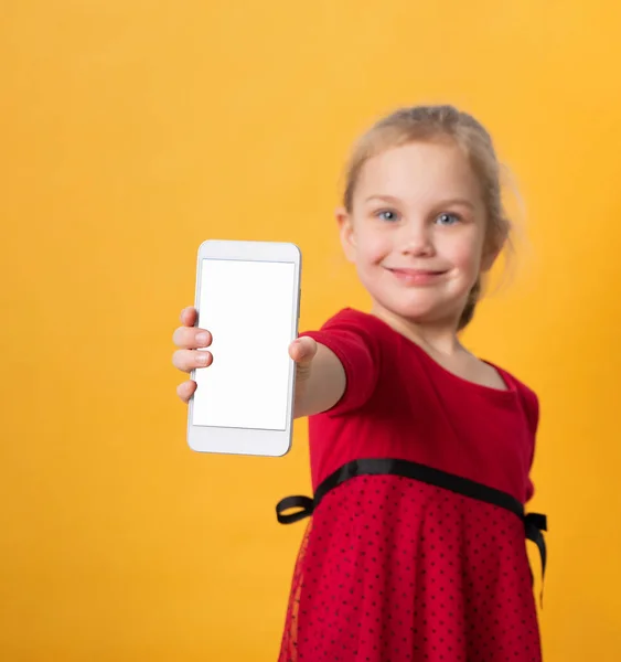 Primer plano retrato de una linda niña sonriente mostrando el teléfono móvil de pantalla en blanco mientras está de pie — Foto de Stock