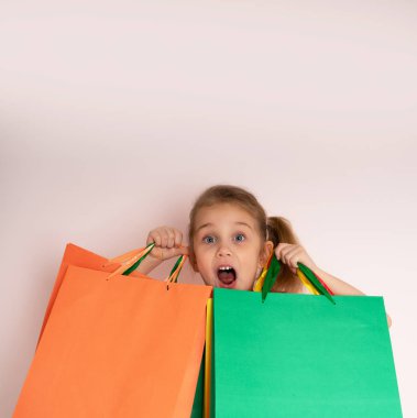 Alışveriş küçük kız kopya alanında ligth arka plan üzerinde yan bakarak alışveriş çantaları tutan..