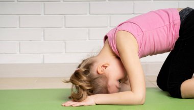 Neşeli küçük kız evde mat spor egzersizleri yapıyor, çocuk spor ve yoga