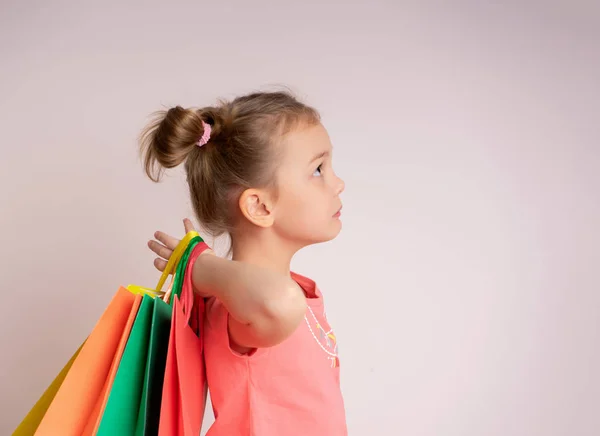 Compras niña sosteniendo bolsas de compras mirando hacia el lado en el fondo de ligth en el espacio de copia .. —  Fotos de Stock