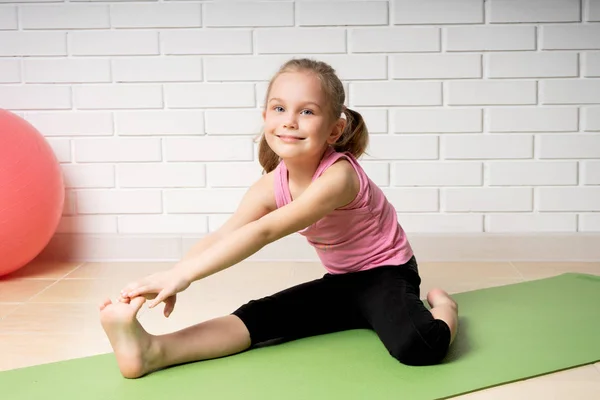 Niña alegre haciendo ejercicios deportivos en la esterilla en casa, deportes infantiles y yoga —  Fotos de Stock