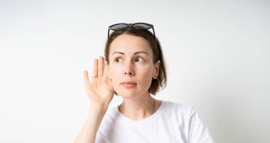 İlgilenen bir kadının kulağına yakın bir el tuttuğu, bilgi dedikodularını dinlediği, beyaz bir tişört giydiği bir kopya alanı olan portresi. gri arka planda yalıtılmış