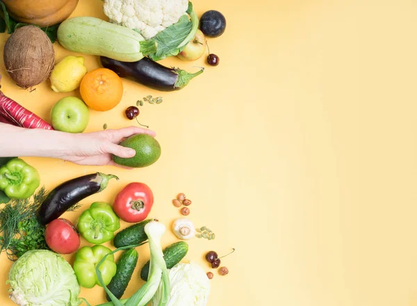 Kvinnlig hand hållande avokado frukt mot bakgrund av frukt och grönsaker, vegan urval, hälsosam mat, ZOH, — Stockfoto