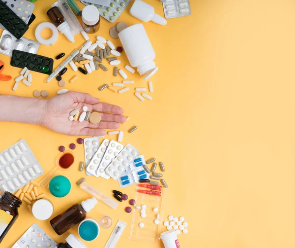 Visão superior da mão feminina segurando pílulas tablet contra fundo amarelo. Muitos comprimidos, comprimidos, medicamentos e outros acessórios médicos . — Fotografia de Stock