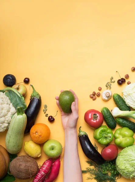 Kvinnlig hand hållande avokado frukt mot bakgrund av frukt och grönsaker, vegan urval, hälsosam mat, ZOH, — Stockfoto