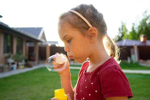 En liten flicka blåser såpbubblor i sommaren park. — Stockfoto