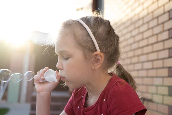 En liten flicka blåser såpbubblor i sommaren park. — Stockfoto