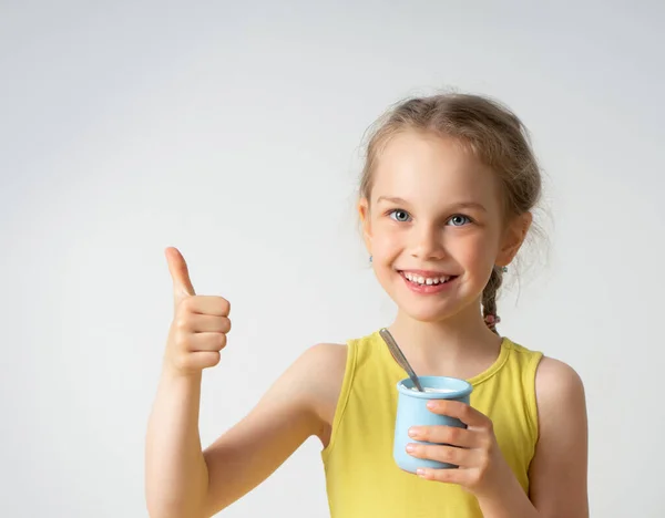 Menina sorridente adorável com uma deliciosa sobremesa na mão olhando para a câmera mostrando o polegar para cima. Close up estúdio retrato isolado em branco — Fotografia de Stock