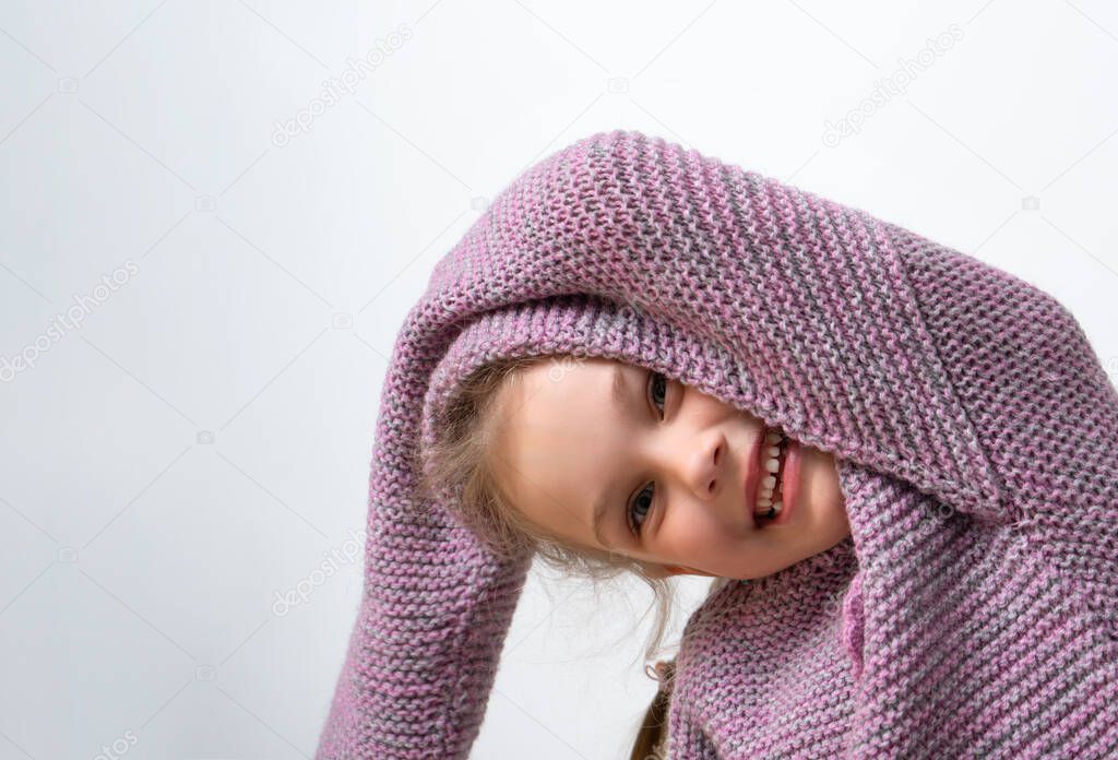 Joyful girl preschooler posing in large knitted lilac sweater, leaning aside with one hand above her head demonstrating long sleeve
