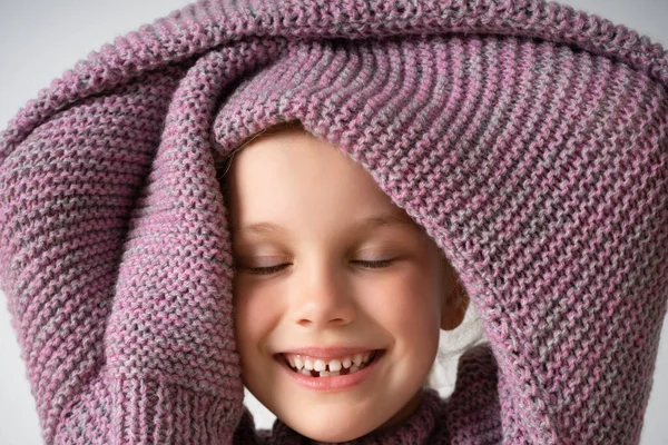 Vista da vicino di una divertente bambina in posa in un maglione a maglia enorme e caldo, sorridente e chiudendo gli occhi in delizia. Studio girato isolato su bianco — Foto Stock