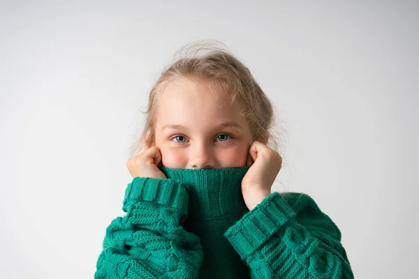 Adorabile bambina che nasconde la parte inferiore del viso sotto il colletto spesso di caldo maglione a maglia. Close up studio girato isolato su bianco, copia spazio — Foto Stock