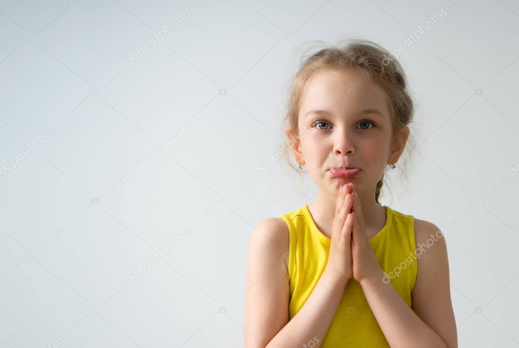 Cute girl preschooler is begging to buy or to give her something folding palms together and pushing her lower lip out, isolated on white
