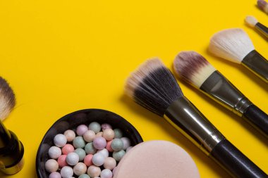 Makyaj fırçası ve kozmetik ürünleri, sarı arka planda izole edilmiş düz yatıyordu