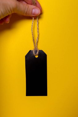 Ellerindeki ipte siyah etiket, sarı arka plan - alışveriş kavramı