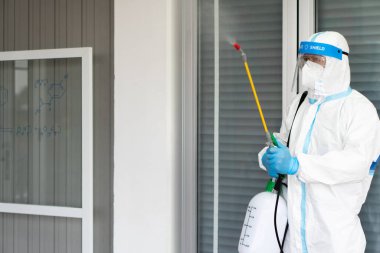 Arındırma servisinde çalışan işçiler koruyucu giysi, yüz kalkanı ve maske de dahil olmak üzere koruyucu ekipman ya da başka bir şey giyiyorlar. Sprey sıkmak için dezenfektan kullanıyor ve laboratuarı temizliyor.