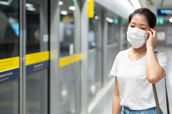 顔のマスクをした若いアジア系の女性がスマートフォンを使ってゲートステーションに立ちCovid 19やコロナウイルスの流行時にスカイ トリアンを待っています 社会的距離と新しい通常の概念は — ストック写真
