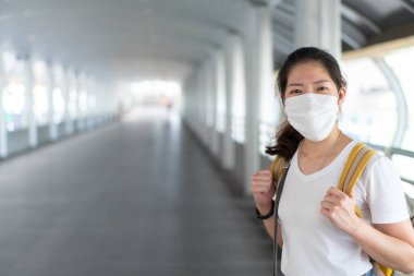 Asyalı genç bir kadın yüz maskesi takıyor, akıllı telefon kullanıyor ve Coperid-19 ya da Coronavirus salgını sırasında şehirde yürüyor. Sosyal uzaklık ve yeni normal yaşam tarzı kavramı