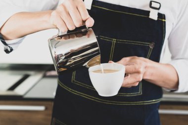 Genç Asyalı bir adam bir fincan kahveye süt döküyor. Kahve ve kahve dükkanı konsepti.