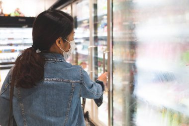 Maske takan genç Asyalı kadın süpermarkette alışveriş yaparken sosyal mesafeyi koruyor. yeni normal, covid-10 ve coronavirus konsepti