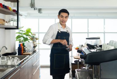 Kafedeki kahve çekirdeklerini öğütmek için kahve makinesini kullanan genç Asyalı adam. barista konsepti