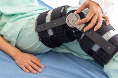 Ortopedi uzmanı, bağların onarılması için yapılan endoskopik ameliyattan sonra hastanın bacağına yerleştirilen diz bağının açısını ayarlıyor. Sağlık ve Tıp Konsepti