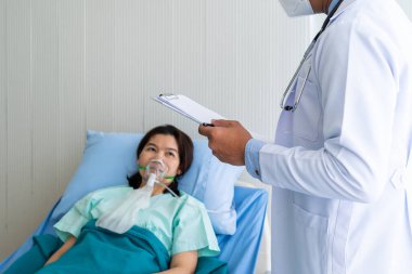 Yüz maskesi takan Asyalı doktor koğuşta hasta olan kadın hastayı ziyaret etti. Sağlık ve Tıp Konsepti