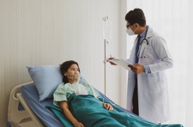 Yüz maskesi takan Asyalı doktor koğuşta hasta olan kadın hastayı ziyaret etti. Sağlık ve Tıp Konsepti