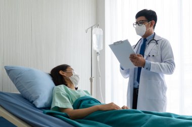 Yüz maskesi takan Asyalı doktor koğuşta hasta olan kadın hastayı ziyaret etti. Sağlık ve Tıp Konsepti